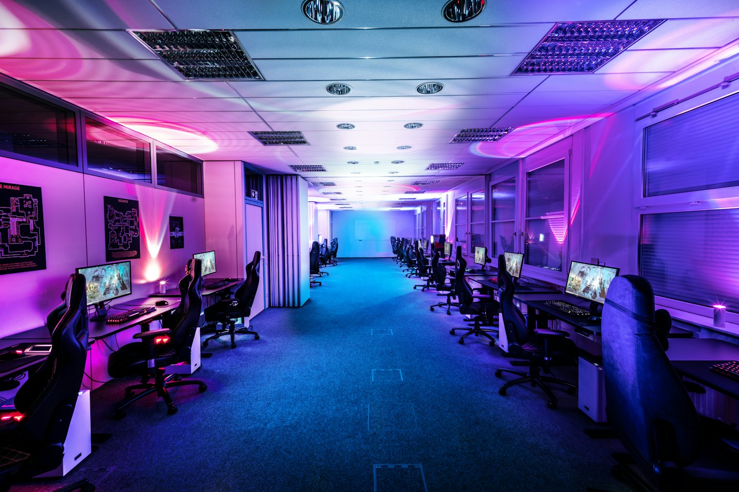 Empty gaming lounge with rows of computers and chairs.